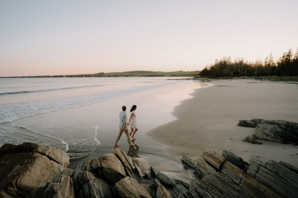 Couple walking on Rissers Beach, Nova Scotia at sunset