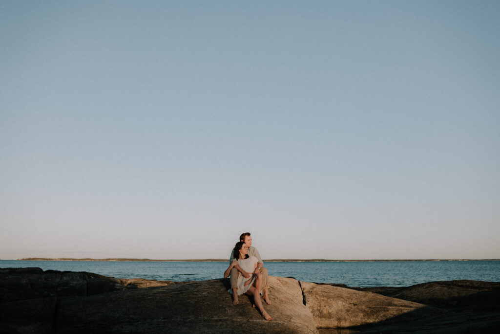 Couple sitting on rock with Atlantic ocean behind them in Halifax, Nova Scotia