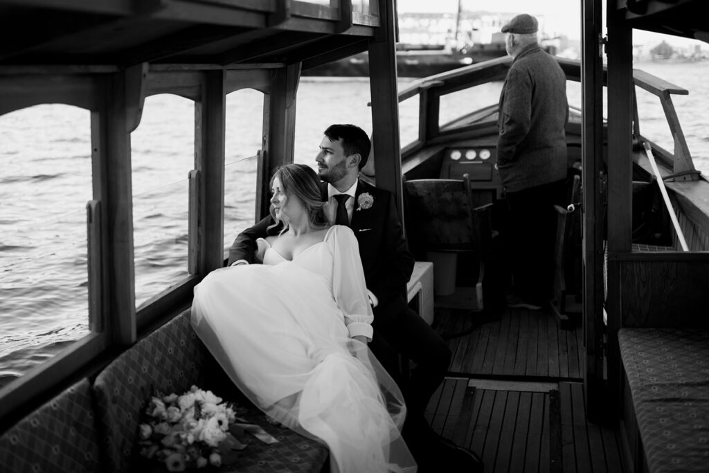 Wedding couple sitting on wooden boat, gazing out to sea off the coast of Halifax