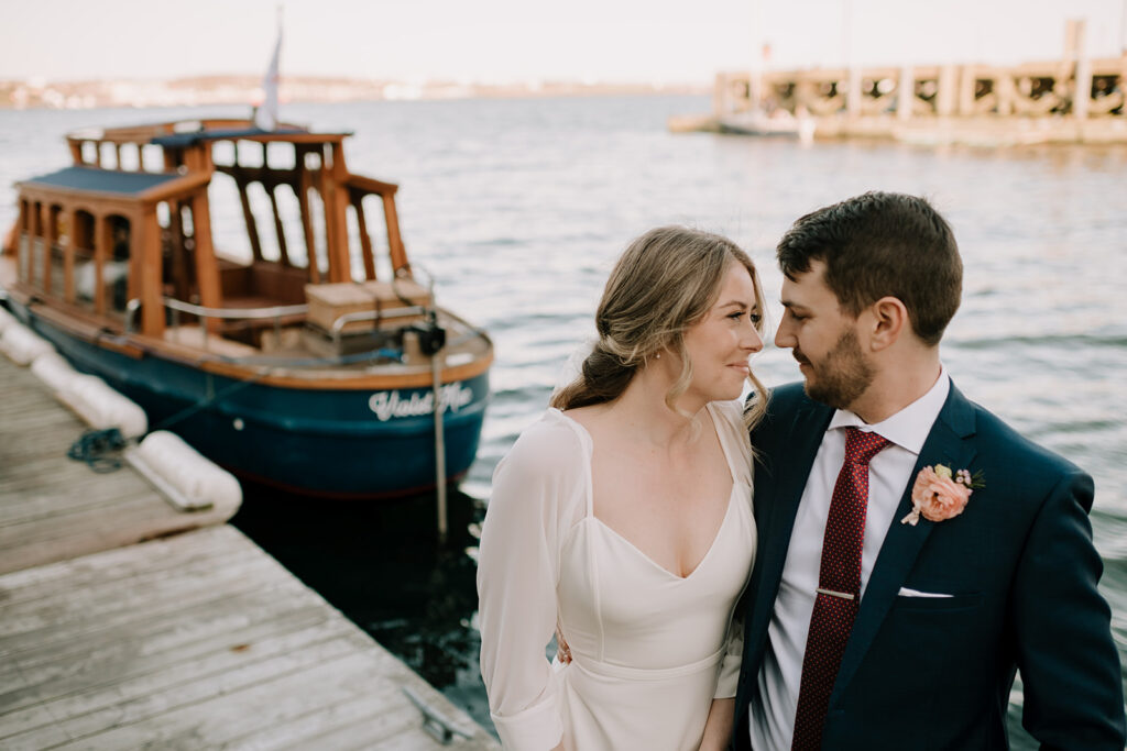Bride and groom gazing into each other's eyes while standing on dock next to boat in Halifax Harbour