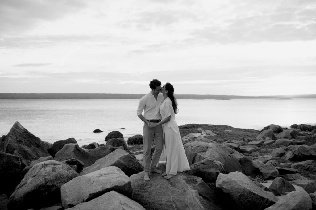 Couple kissing on the rocky shore at Bull Point Estate in Nova Scotia with ocean backdrop.
