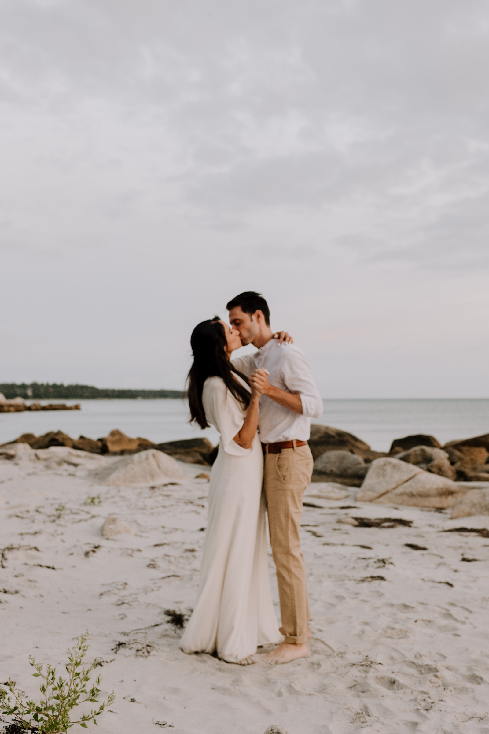 Candid moment of couple kissing during sunset engagement session on the beach in Nova Scotia.