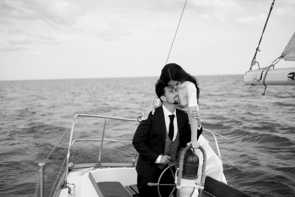 Candid moment of bride and groom sailing away after wedding on sailboat in Halifax, Nova Scotia.